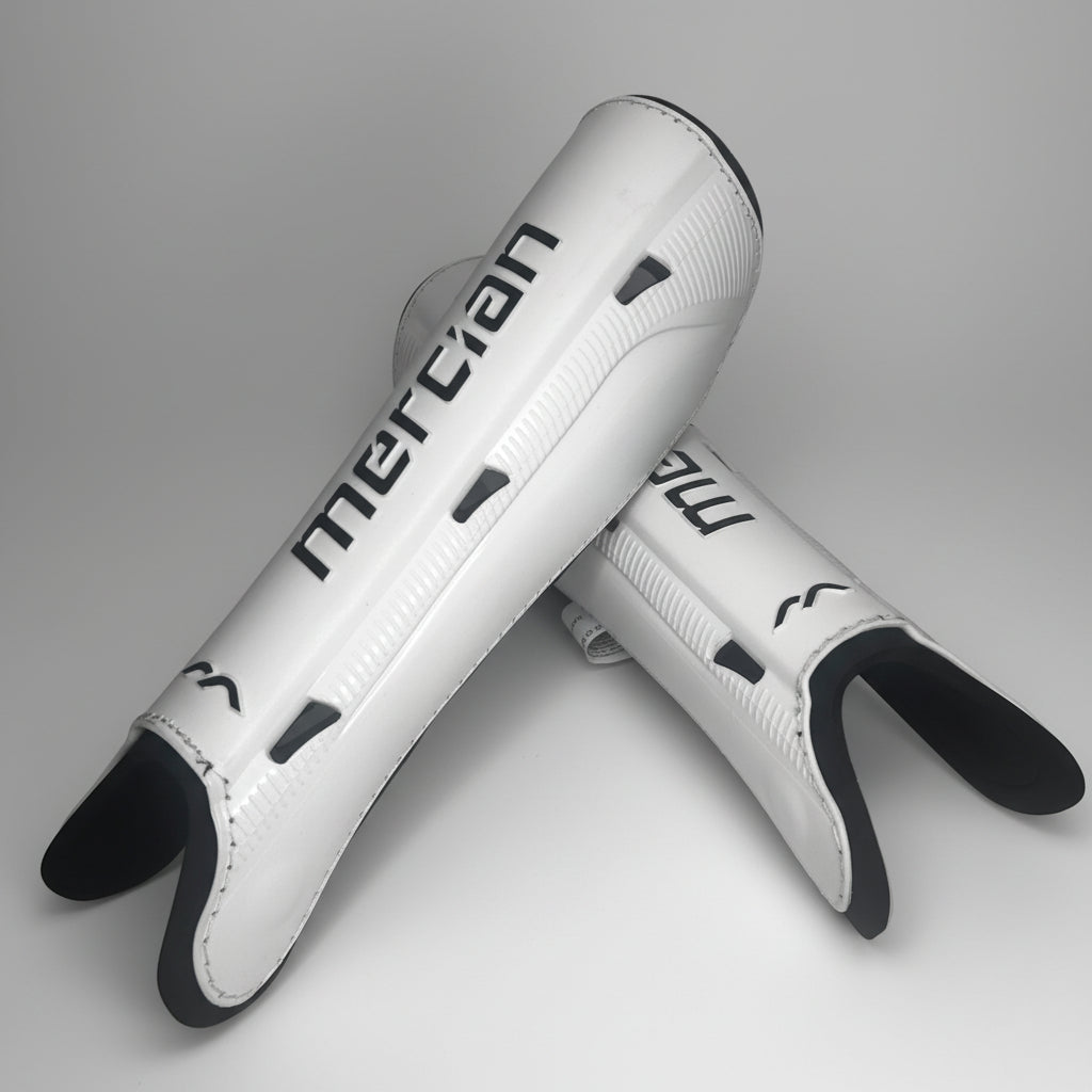 A pair of white Field Hockey shin guards with black accents and the Mercian brand name printed in black, displayed on a light gray background.