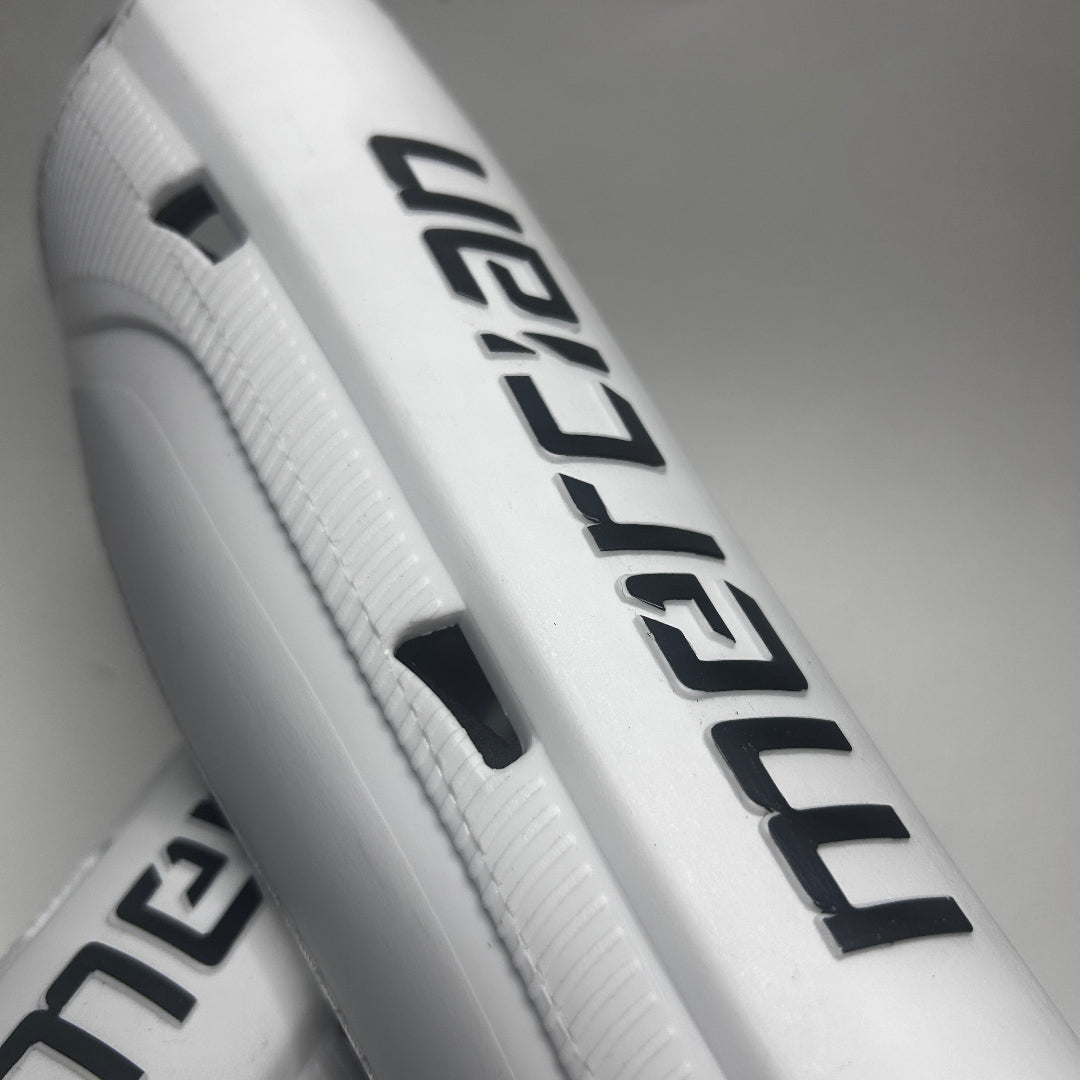 Close-up of a white field hockey shin guard with bold black 'Meridian' branding, showing the textured side panel and ventilation cutouts.