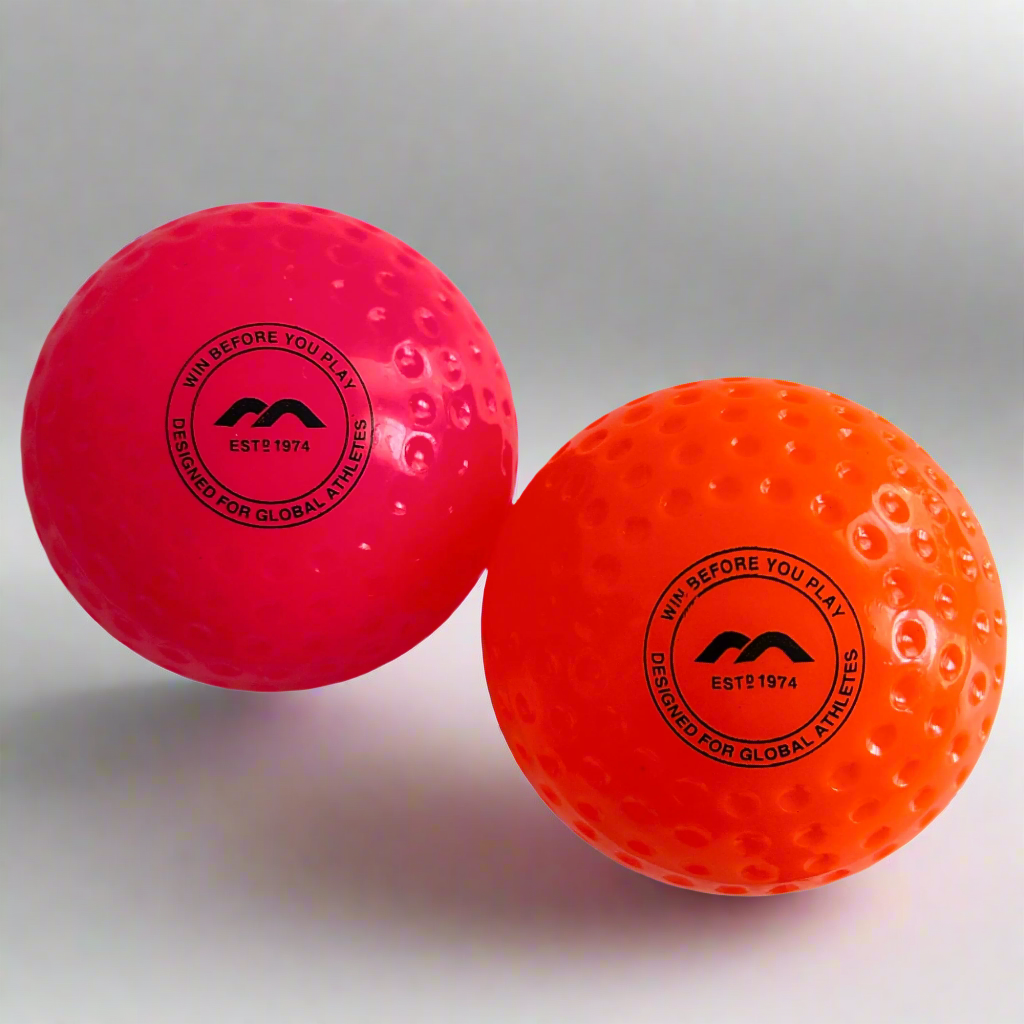 Two field hockey balls, one pink and one orange, with a brand logo on a gray background.