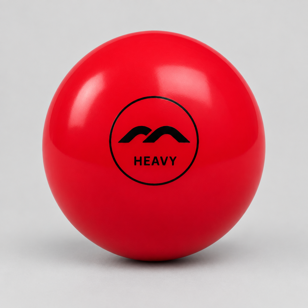 A glossy red field hockey ball with a black circular logo featuring stylized peaks and the word 'HEAVY' in the center, photographed on a light gray studio background.