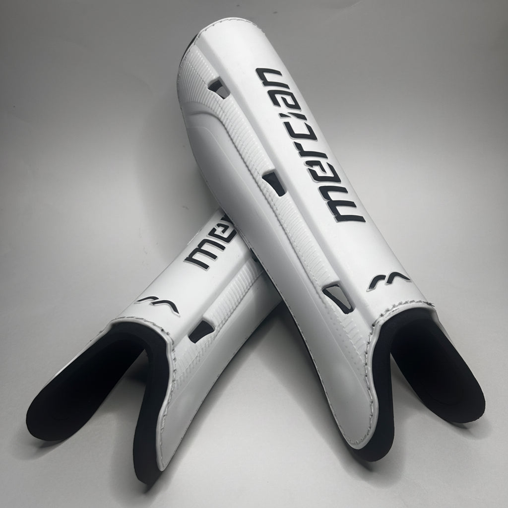 A pair of white shin guards with black accents and the brand name 'mercian' printed in black on the front, displayed on a neutral gray background.